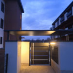 Tettoia sospesa con struttura in tubolare e lamiera tagliato al laser sorretta da quattro piantoni a copertura di uno degli ingressi con cancelletto pedonale in lamiera tagliata al laser e maniglione in acciaio inox e realizzazione della copertura per i contatori il tutto zincato e verniciato con illuminazione led di sera